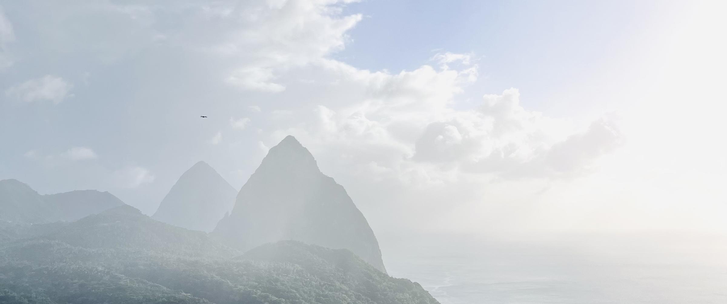 The Pitons half hidden in sea mist, with a frigatebird crossing the sky